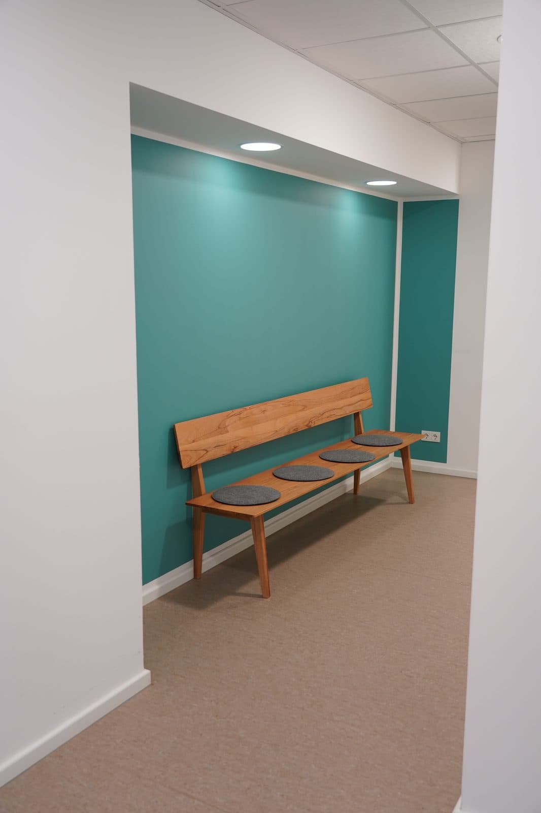 Wartebereich mit Holzbank vor türkiser Akzentwand